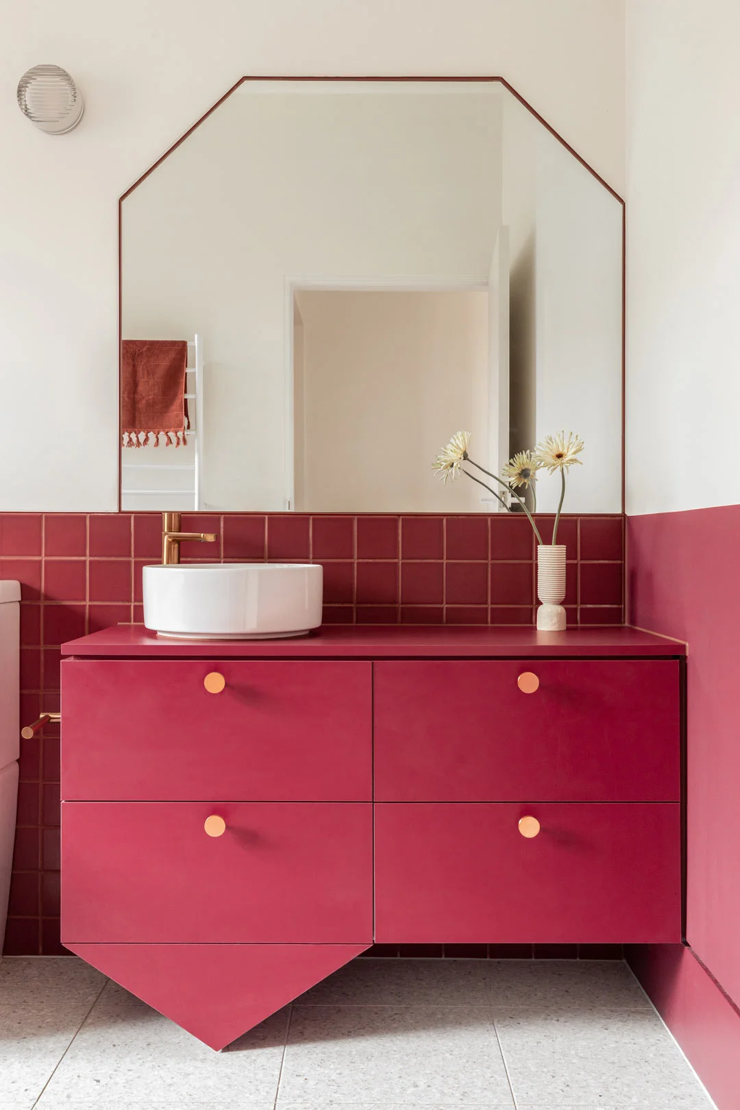 A bright modern art deco bathroom with magenta cabinetry and brished copper tapware