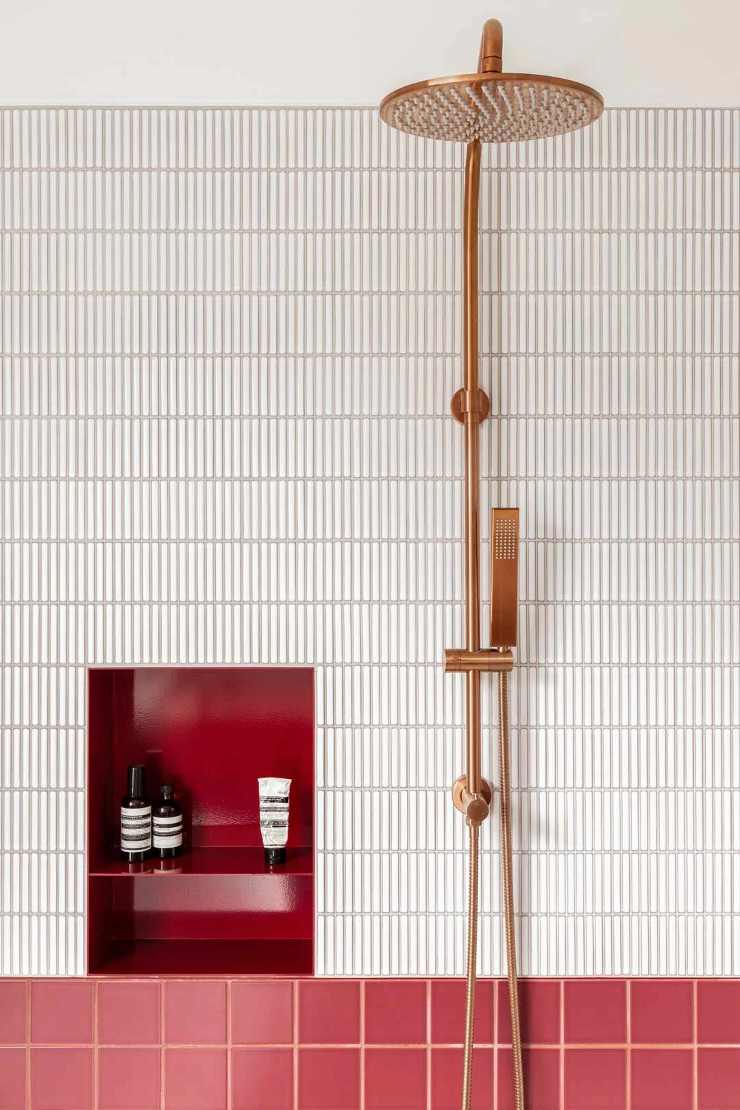 Magenta coloured feature tiles paired with white kit kat tiles and brushed copper shower set
