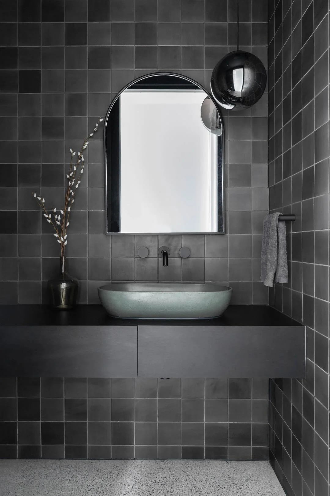 Matte black tapware a dark green basin and black cabintry paired with black tiles for a dark interior design bathroom